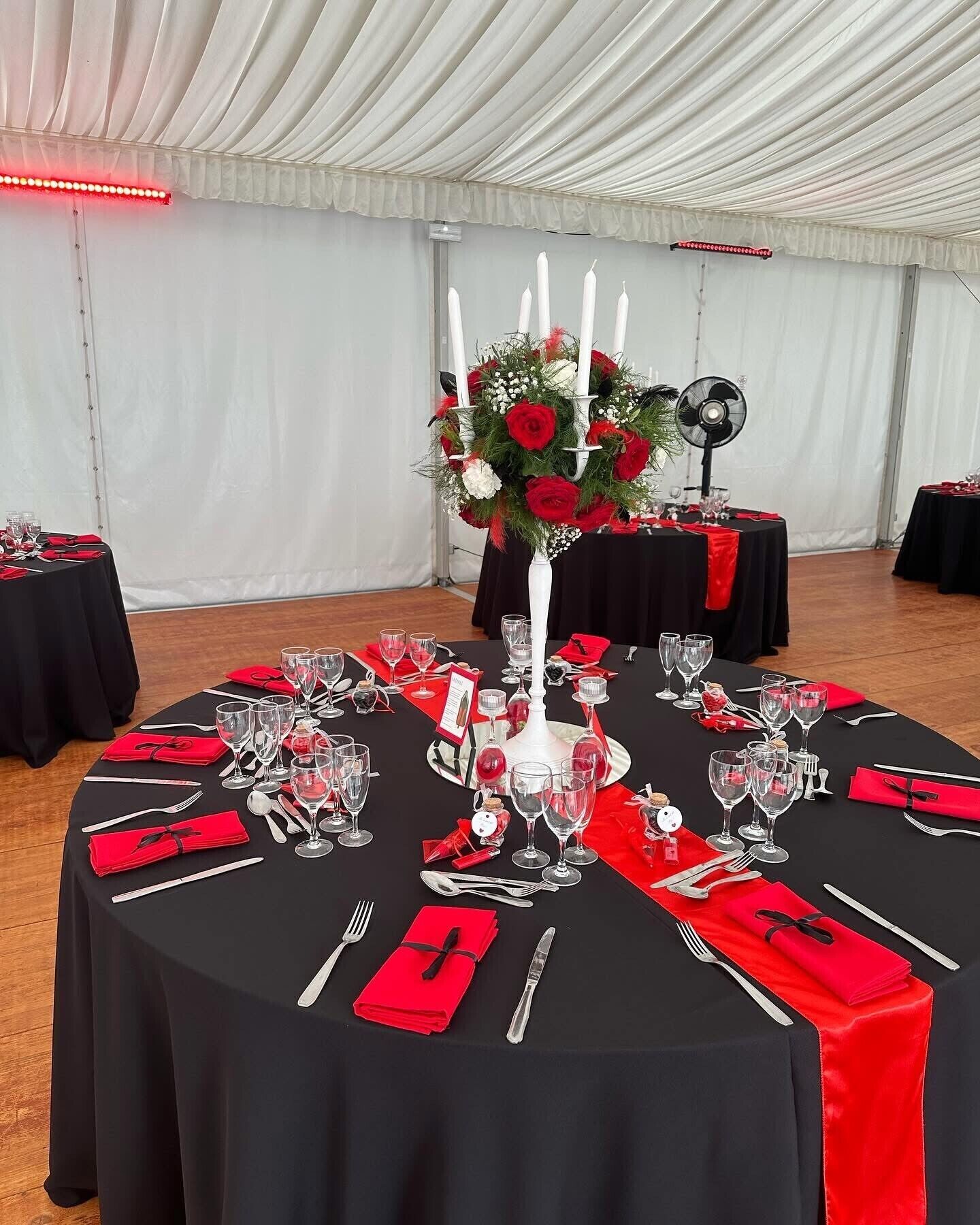 A round table set for a formal event with black tablecloths, red napkins, and a centerpiece with red roses and white candles.