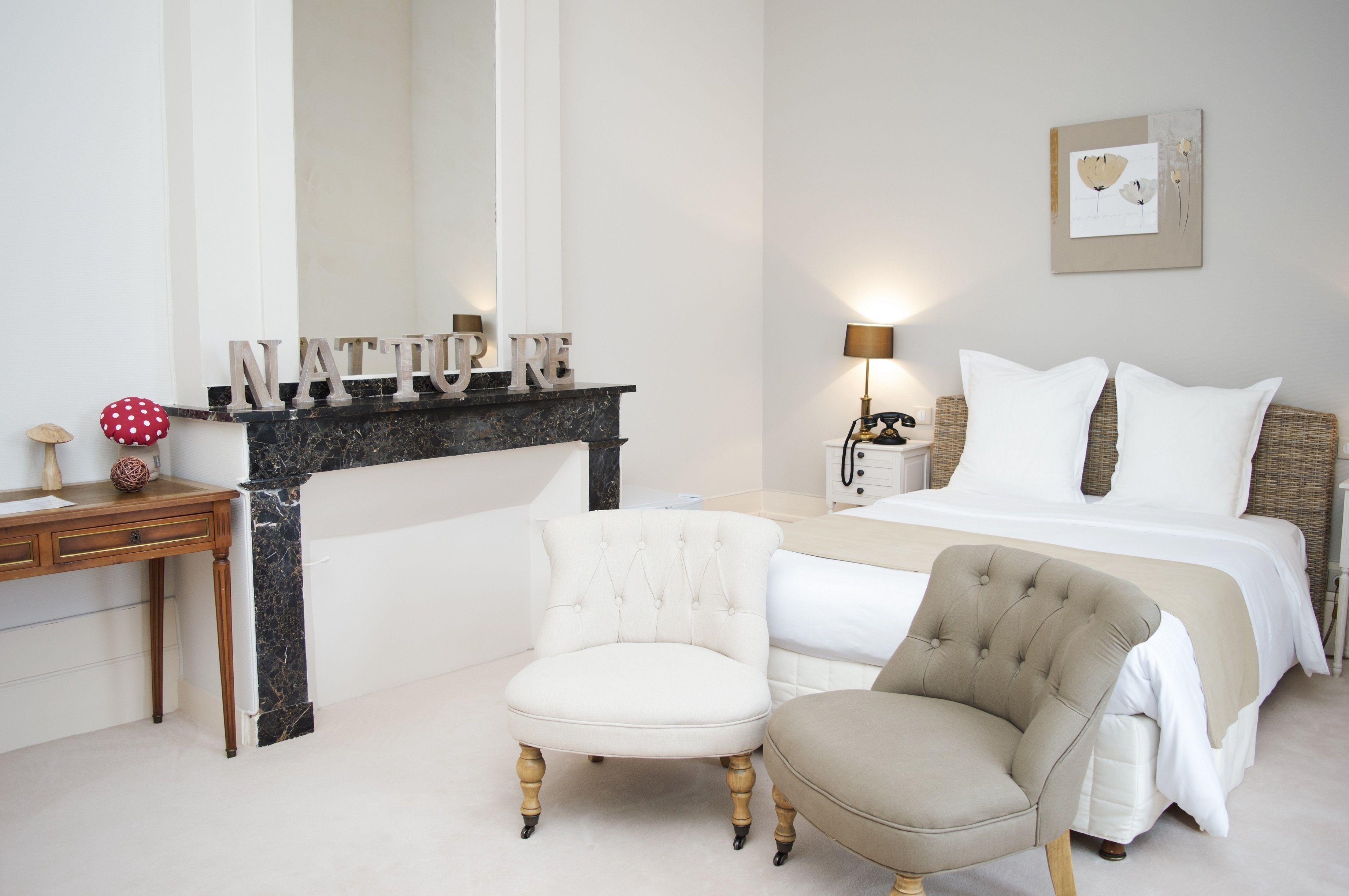 A bedroom with a bed, two chairs, a nightstand, a lamp, and a fireplace with the word "NATURE" on it.