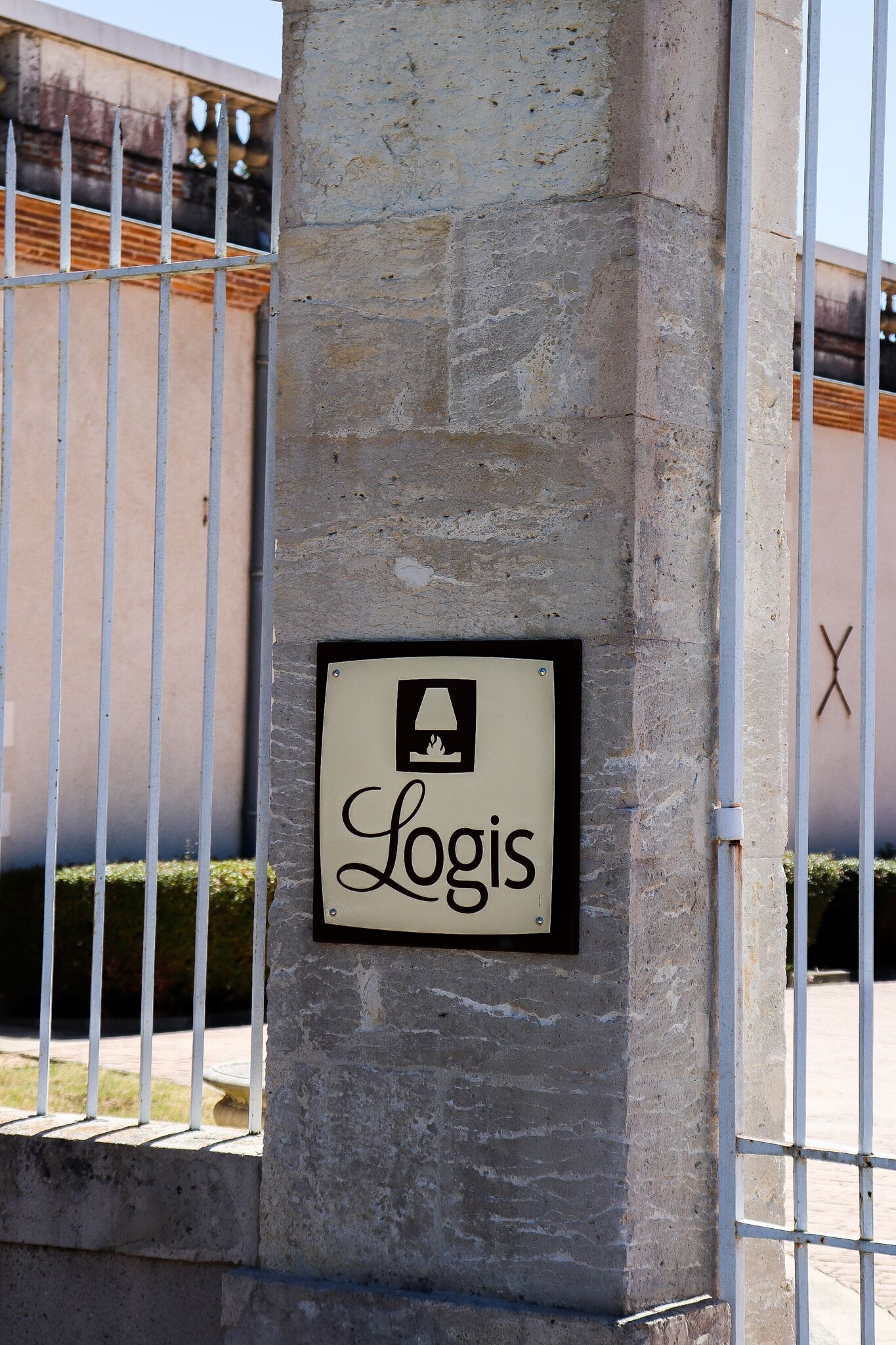 Une pancarte sur un pilier de pierre, portant le mot « Logis » et un symbole représentant un lit, indiquant un hôtel ou un établissement proposant des hébergements.