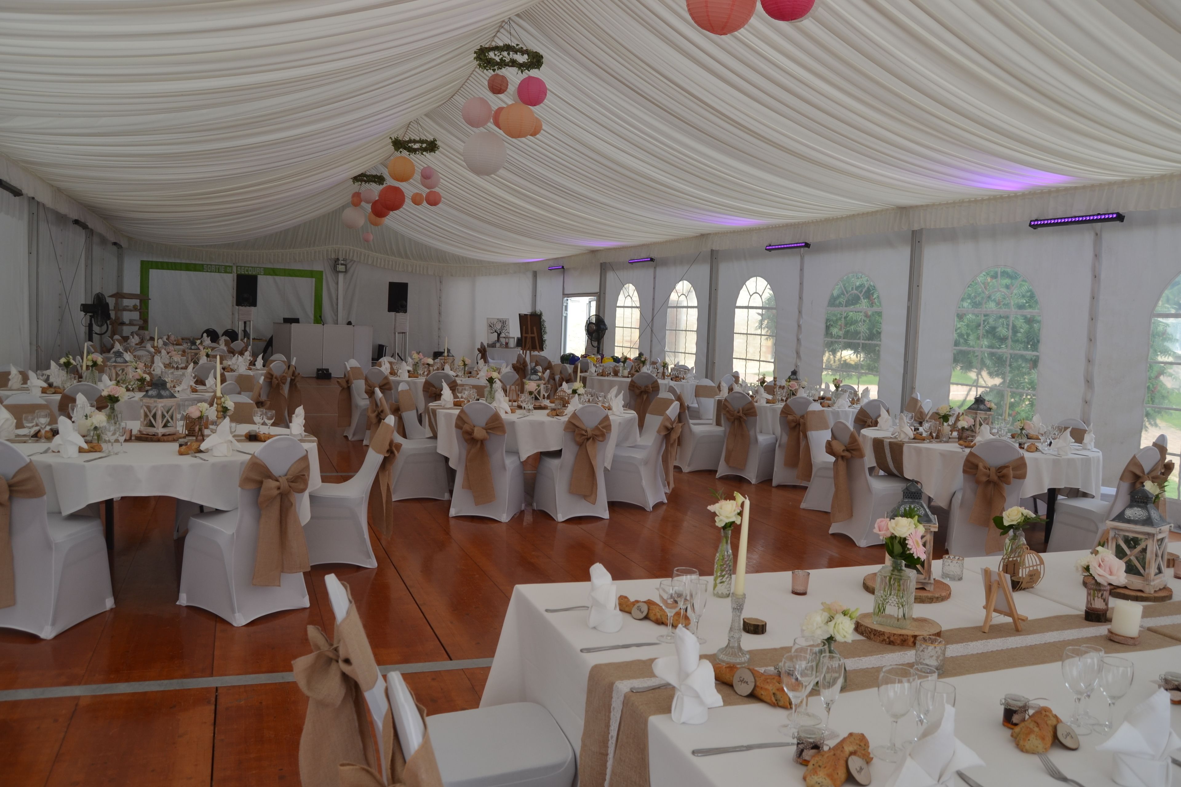 A large hall with white tables and chairs, adorned with white tablecloths and brown sashes.