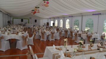A large hall with white tables and chairs, adorned with white tablecloths and brown sashes.