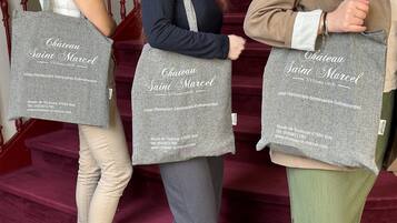 Three individuals carrying grey tote bags with 'Château Saint Marcel' branding and contact information.