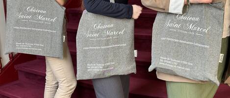 Three individuals carrying grey tote bags with 'Château Saint Marcel' branding and contact information.
