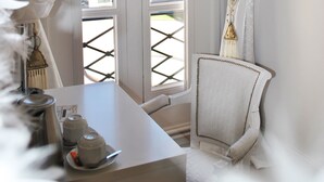 Ein Zimmer mit einem weißen Sessel, einem Tisch mit einer Lampe und Blick durch ein Fenster mit Vorhängen.