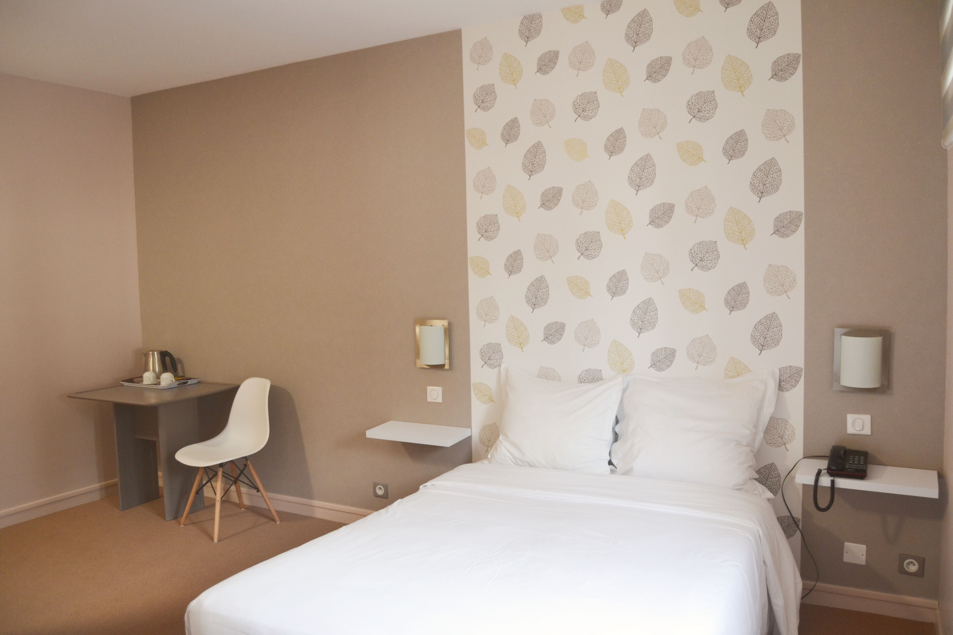 A hotel room with a bed, a desk, a chair, and a wall with a leaf pattern.