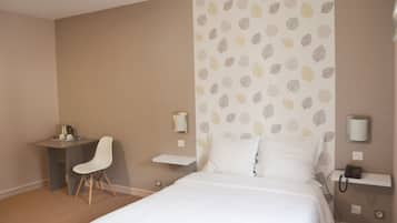 A hotel room with a bed, a desk, a chair, and a wall with a leaf pattern.