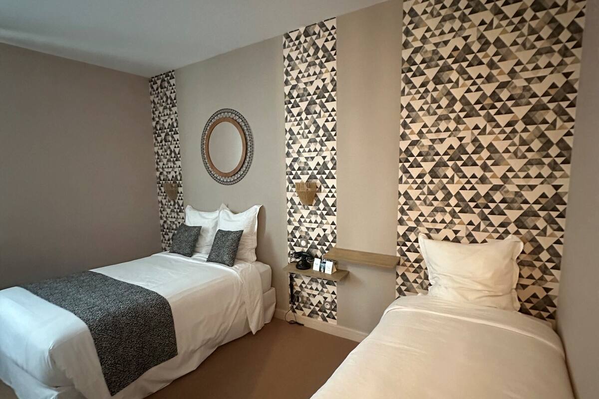 A hotel room with two beds, a mirror, a wall-mounted shelf, and a patterned wall.