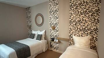 Une chambre d’hôtel avec deux lits, un miroir, une étagère fixée au mur et un papier peint à motifs.