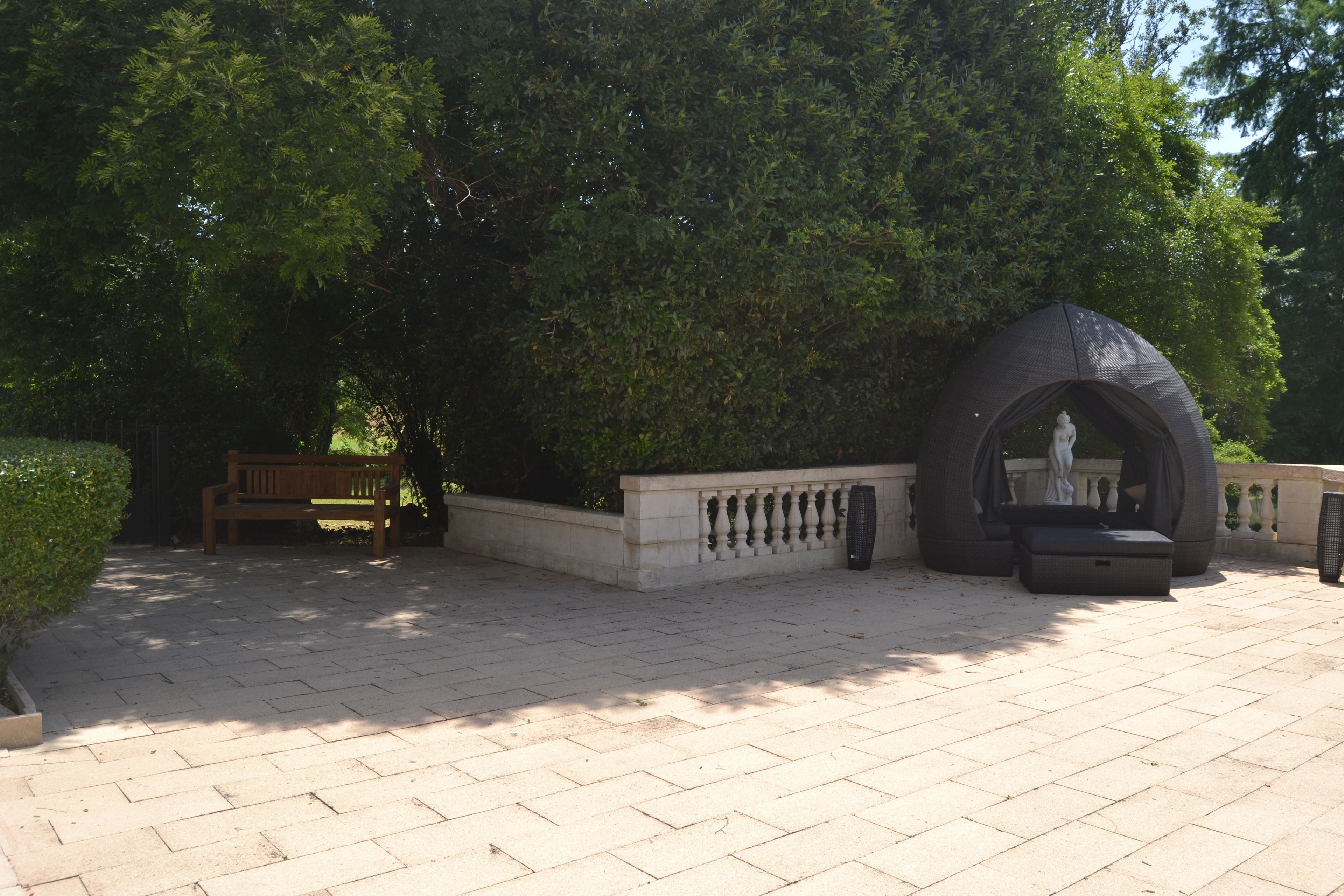 A paved outdoor area with a bench, a statue, and a large, semi-circular structure.
