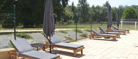 A series of wooden lounge chairs with grey cushions and matching umbrellas, arranged on a tiled patio area.