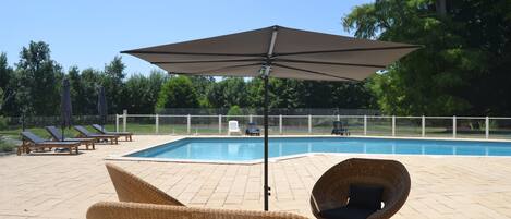 A poolside area with lounge chairs, a large umbrella, and a swimming pool.