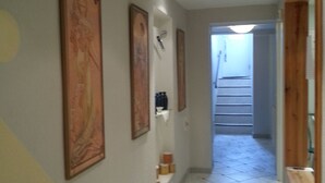 Ein Flur mit Fliesenboden, gerahmten Kunstwerken an den Wänden und einer Treppe am Ende.