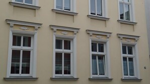 Ein mehrgeschossiges Gebäude mit einer symmetrischen Fassade, versehen mit gleichmäßig angeordneten Fenstern in weißen Rahmen und dekorativen Gesimsen.