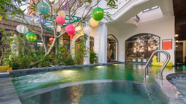 An indoor swimming pool with a fountain, surrounded by plants and colorful lanterns. - Hoang Trinh Hotel (Da Nang)