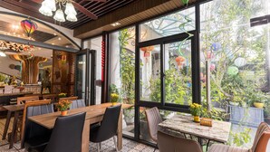 A restaurant with a large window, wooden tables, and black chairs. - Hoang Trinh Hotel (Da Nang)