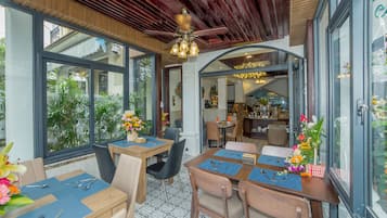 A dining area with tables set for four, large windows, and a ceiling fan.