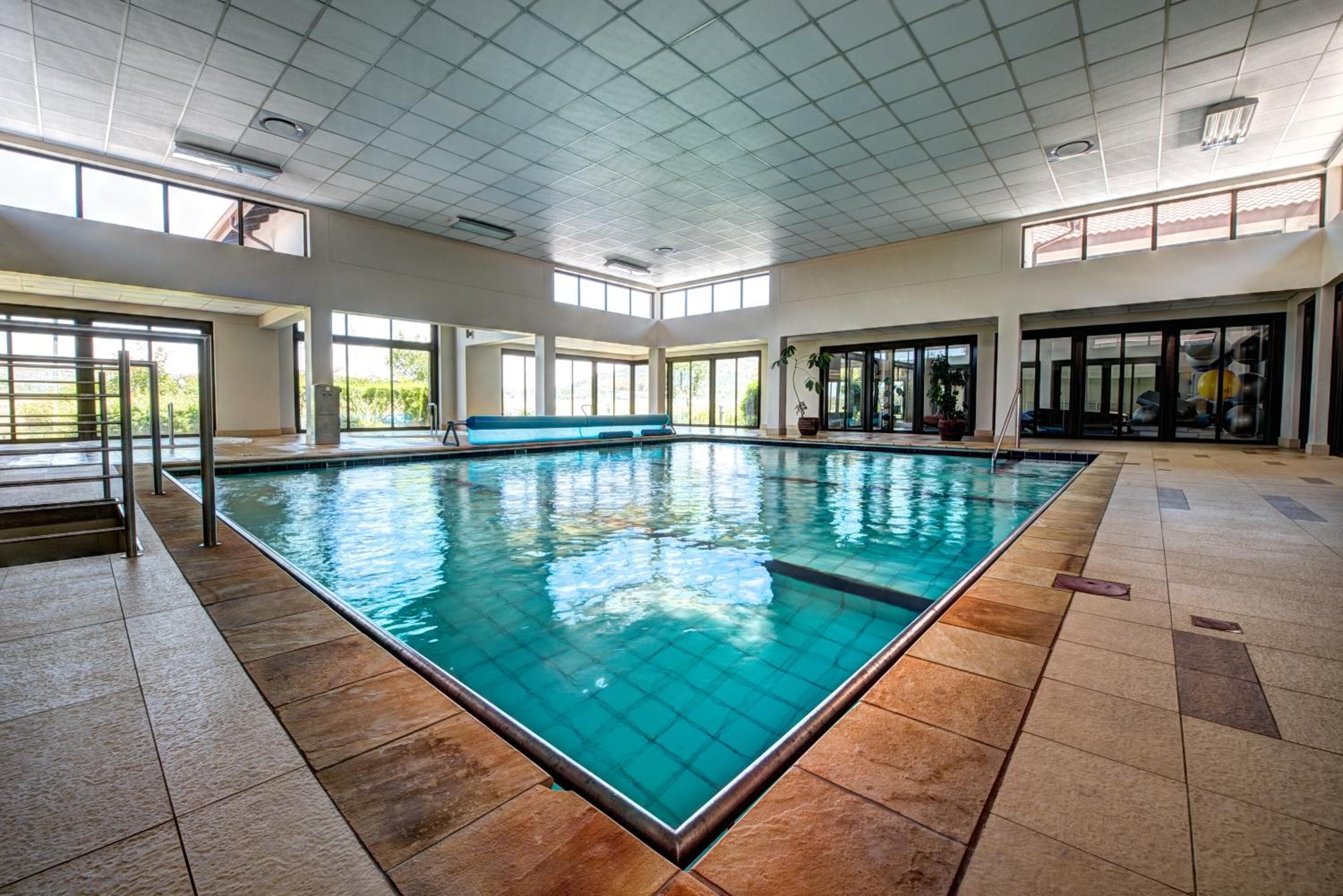 An indoor swimming pool with clear glass walls, a tiled floor, and a bench along the side.