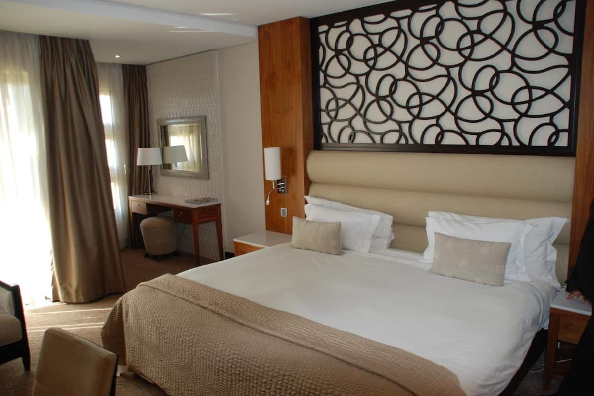 Une chambre d’hôtel avec un grand lit, un bureau, une chaise, un miroir et un panneau décoratif mural.