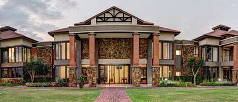 A large, multi-story building with a symmetrical facade, featuring a central entrance with a glass door and a stone wall.