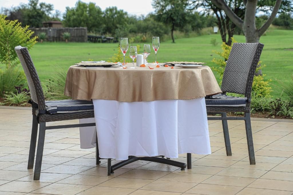 An outdoor dining table set with a tablecloth, chairs, and wine glasses.