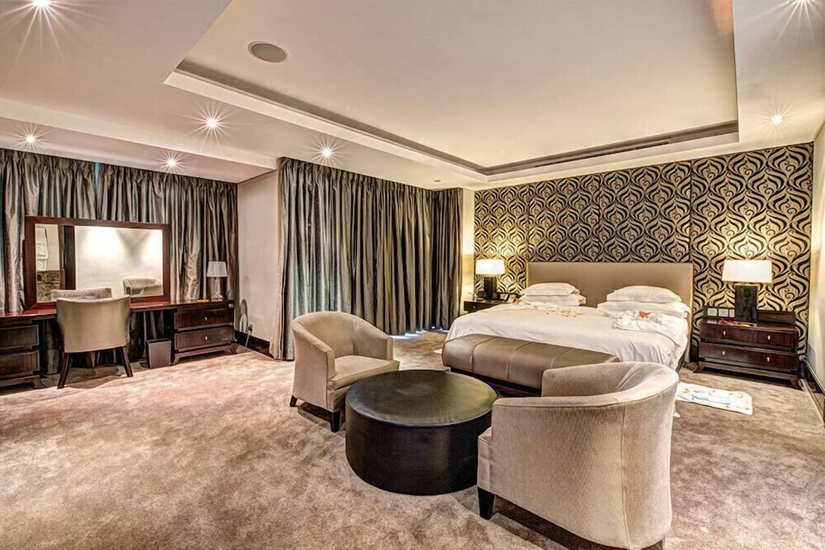 Une chambre d’hôtel avec un grand lit, deux fauteuils, un bureau et une table basse ronde.