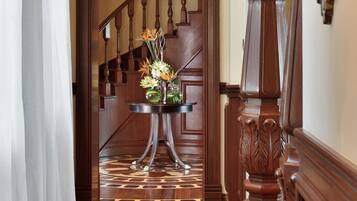 A wooden staircase with a chandelier, a round table with flowers, and a patterned rug.