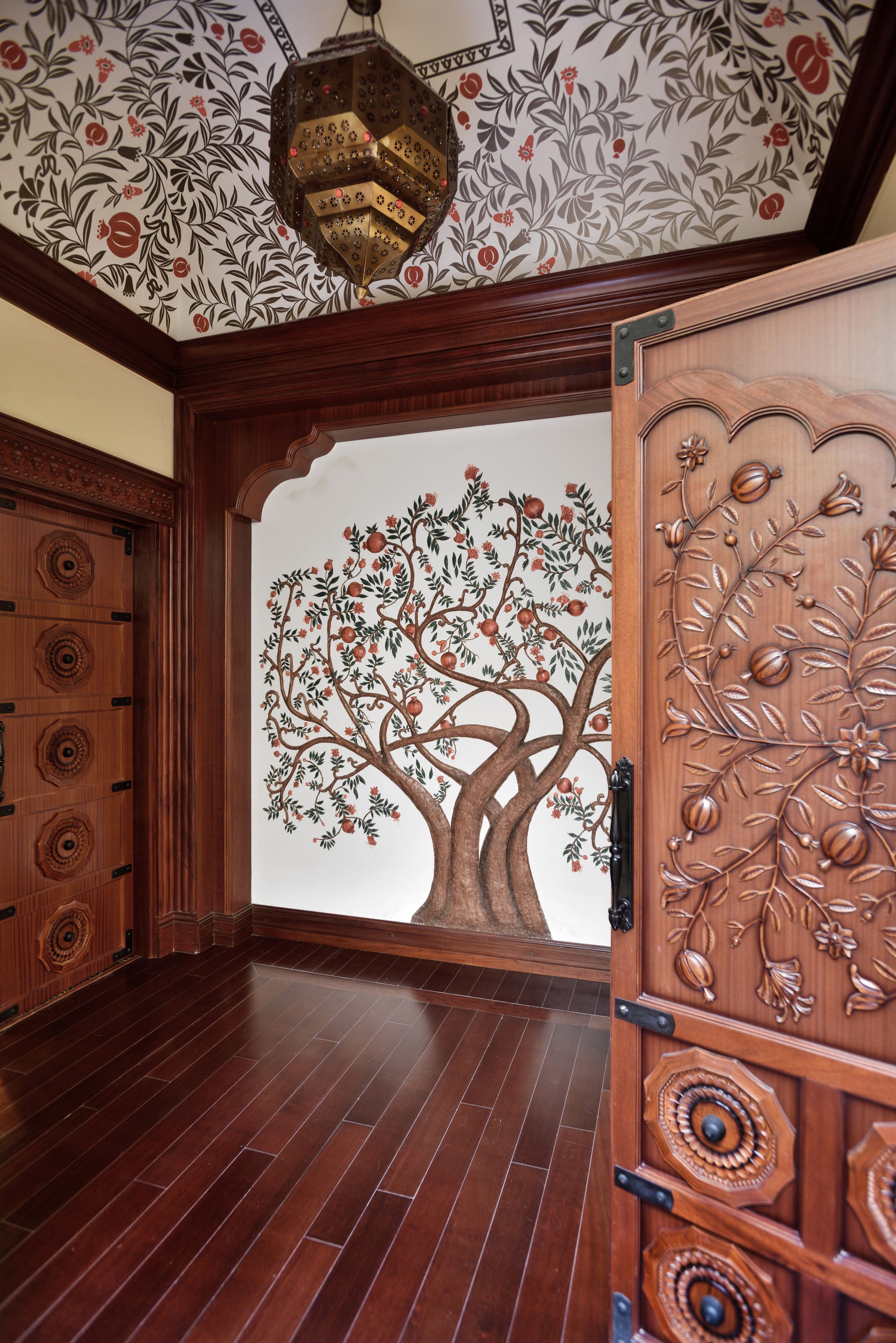 Une pièce dotée d’un plancher en bois, d’une porte décorative ornée d’un motif d’arbre et d’un plafond à motifs.
