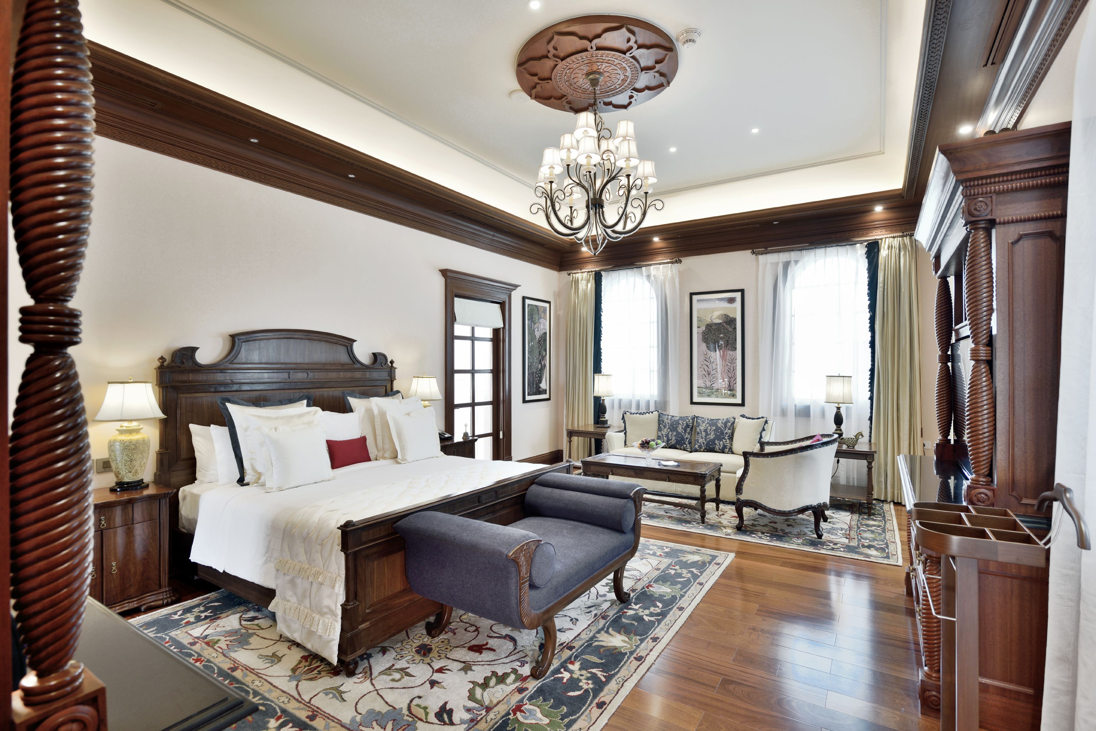 A spacious bedroom with a large bed, a sitting area with a sofa and armchairs, and a chandelier.