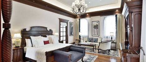 A spacious bedroom with a large bed, a sitting area with a sofa and armchairs, and a chandelier.
