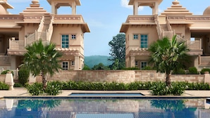 A pool with a person in the water, surrounded by a large building with multiple domes and balconies, and a clear sky in the background. - ITC Grand Bharat, a Luxury Collection Retreat, Gurgaon (Taoru)