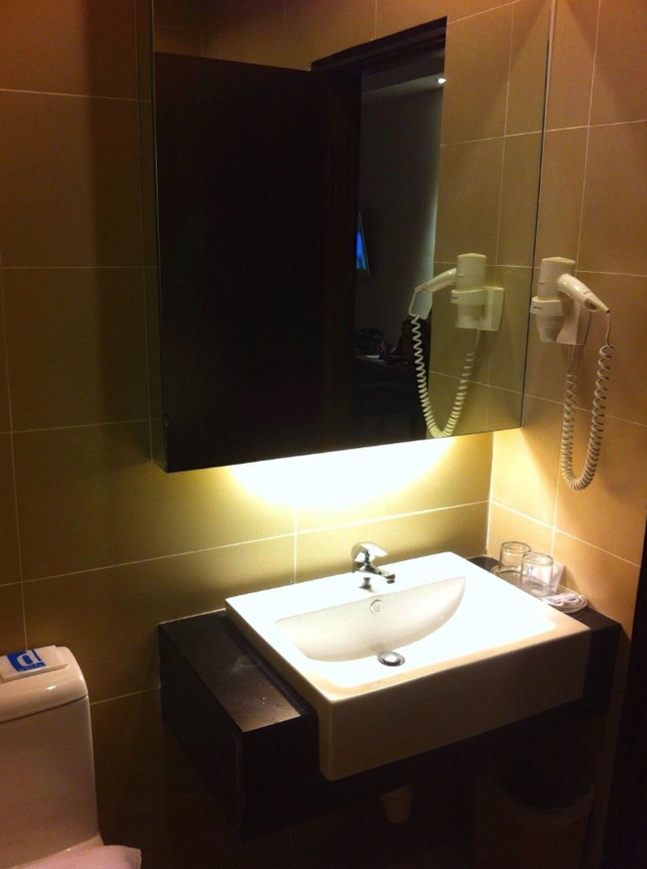 Un baño con un lavamanos blanco, un espejo y un secador de pelo montado en la pared.