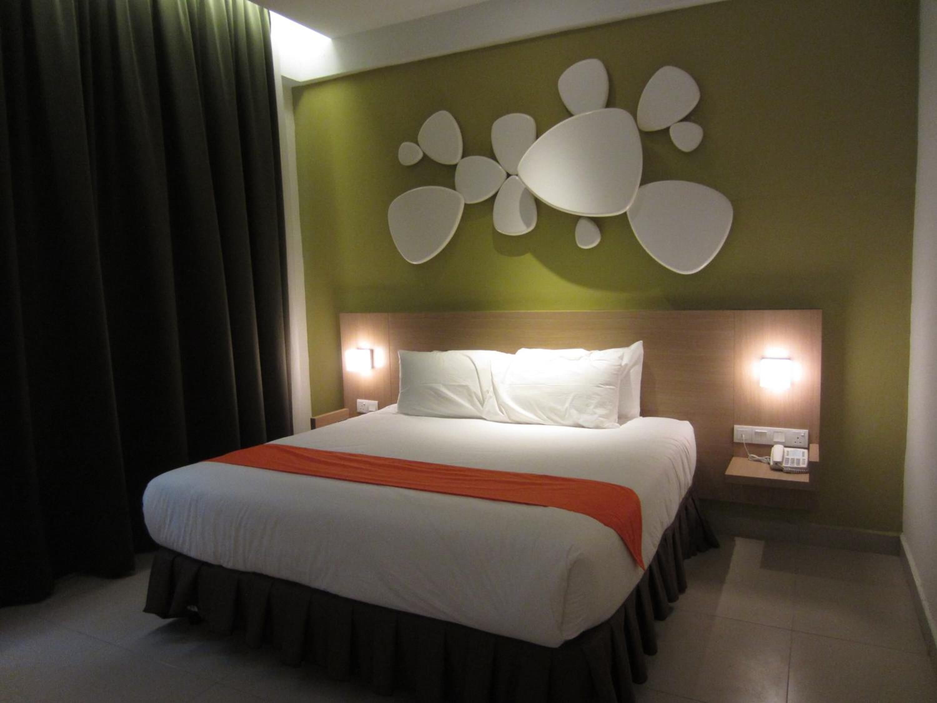 A hotel room with a bed, two bedside tables, a wall-mounted light fixture, and a curtain.