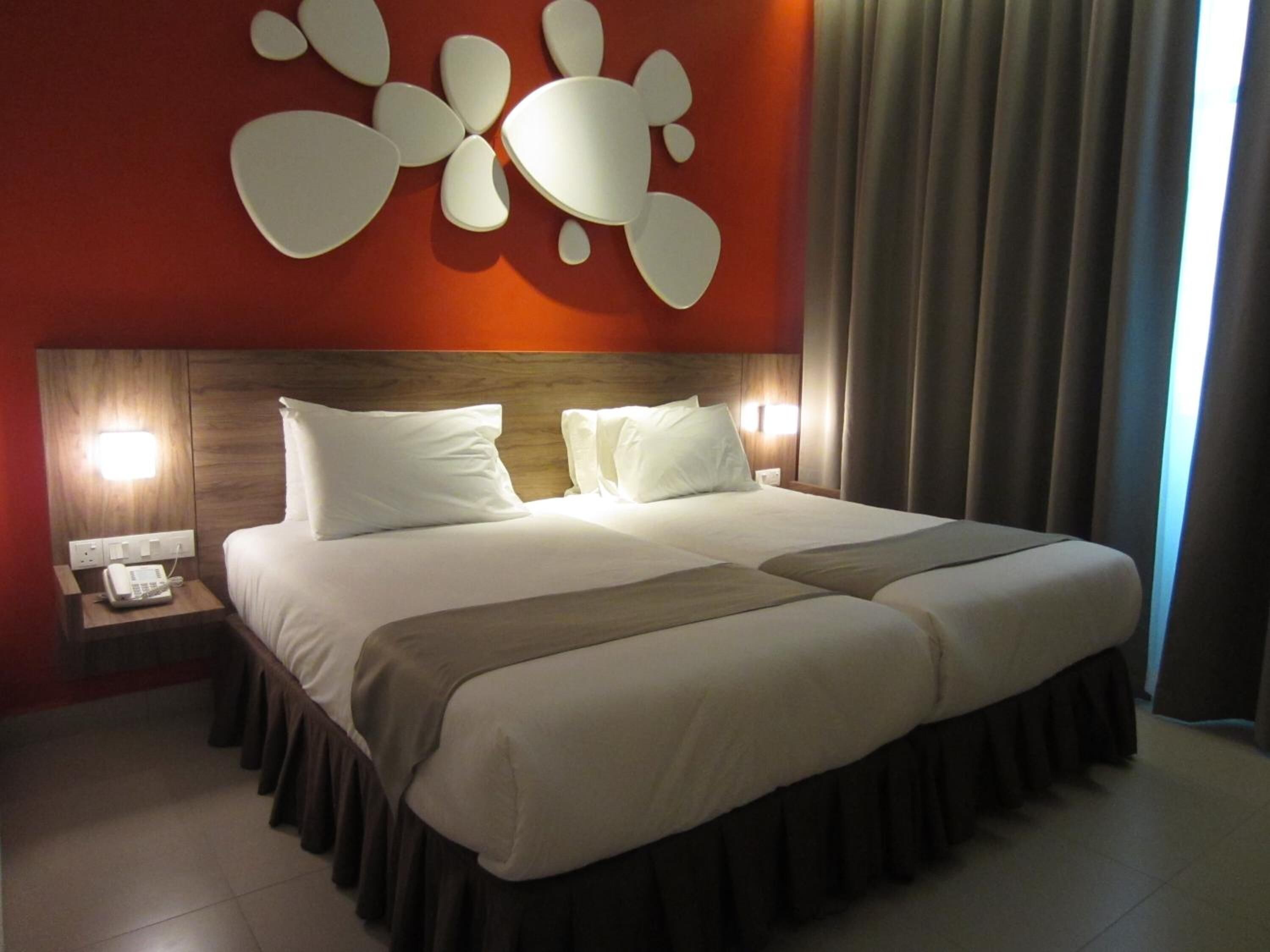 Habitación de hotel con una cama grande, una mesita de noche con teléfono y una pared decorada con arte abstracto.