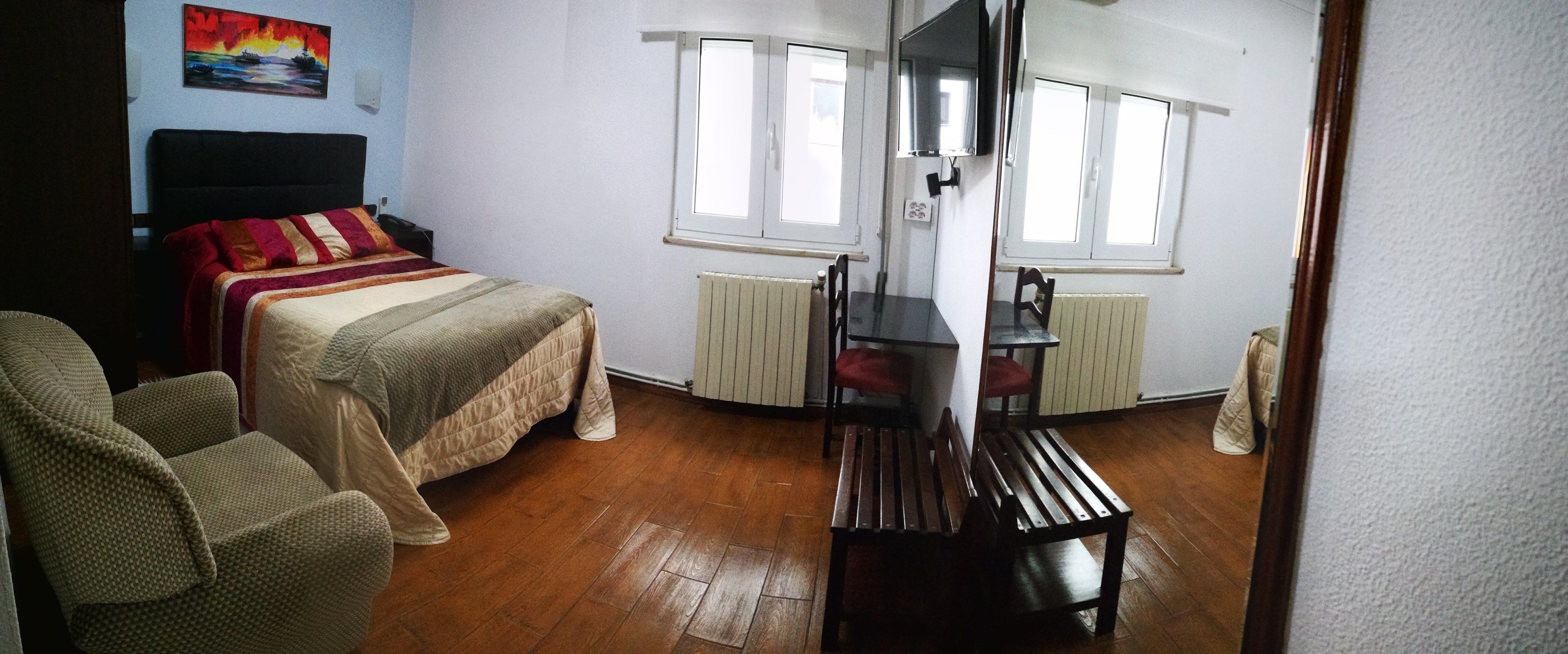 A bedroom with a bed, a chair, a wooden bench, and a TV.