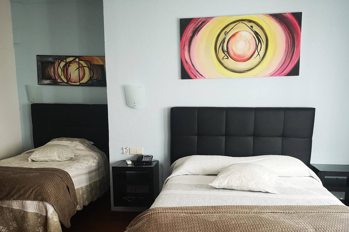 A hotel room with two single beds, a large abstract painting on the wall, and a bedside table with a phone.