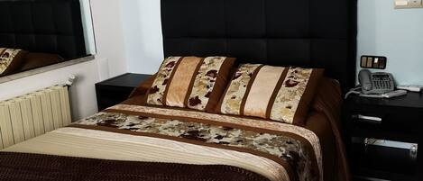 A bedroom with a large bed, a nightstand with a phone, and three framed paintings on the wall.