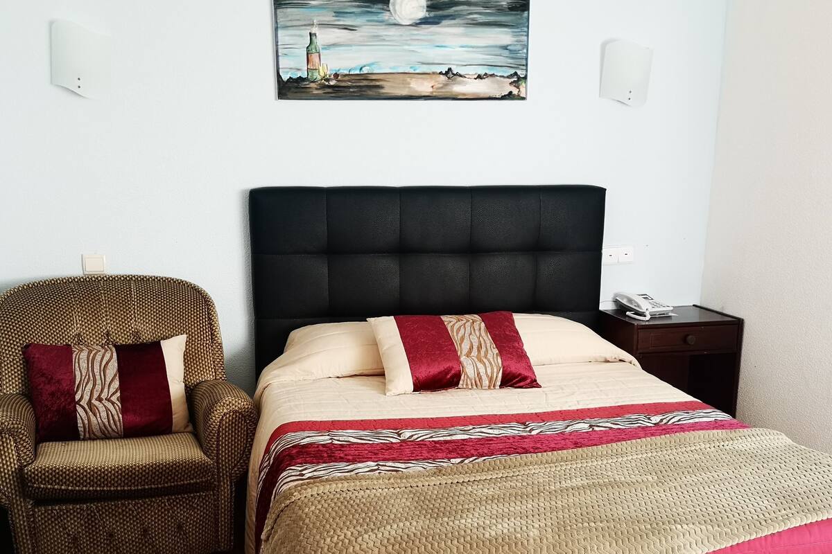 A bedroom with a bed, a chair, a painting, and a nightstand.