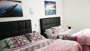 Habitación de hotel con dos camas, cada una con cabecero y almohadas. Hay lámparas fijadas en la pared y un cuadro sobre las camas.