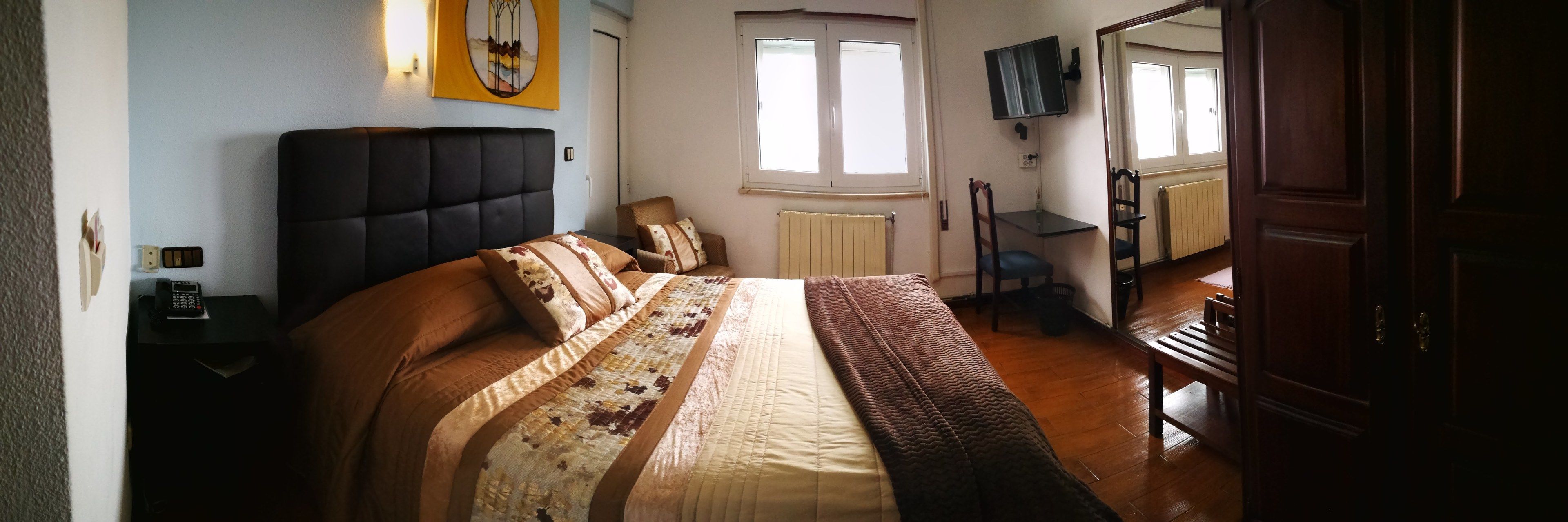 A bedroom with a large bed, a bedside table with a phone, a chair, a radiator, and a TV on the wall.