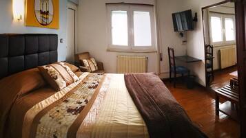 Ein Schlafzimmer mit einem großen Bett, einem Nachttisch mit Telefon, einem Sessel, einer Heizung und einem an der Wand befestigten Fernseher.