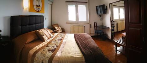 A bedroom with a large bed, a bedside table with a phone, a chair, a radiator, and a TV on the wall.