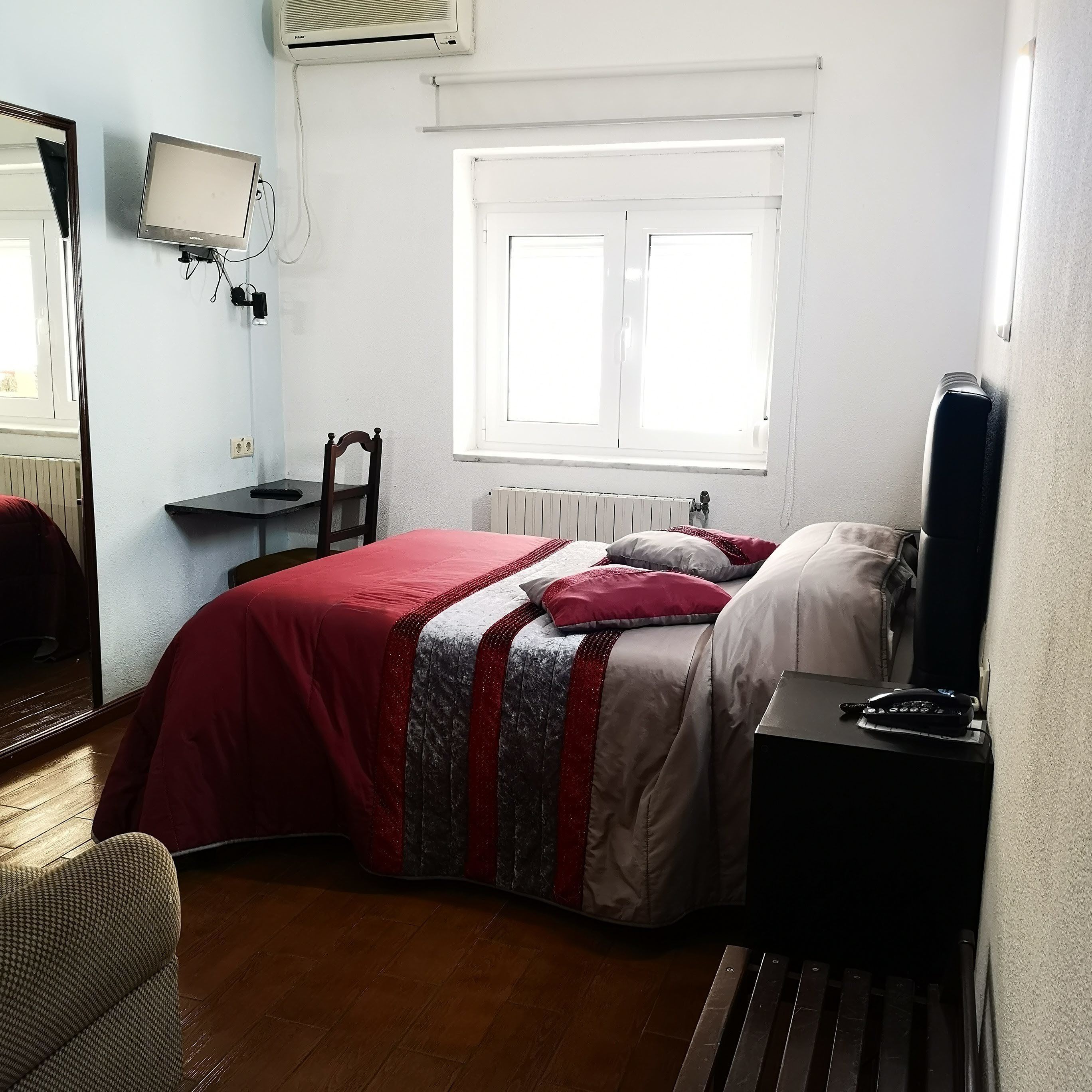 A bedroom with a bed, a chair, a desk, a window, and a radiator.