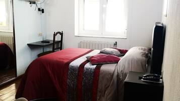 A bedroom with a bed, a chair, a desk, a window, and a radiator.