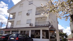 Un hotel blanco de varios pisos con balcones, un letrero visible que dice 'SOFAS BONITOLAR' y coches estacionados.