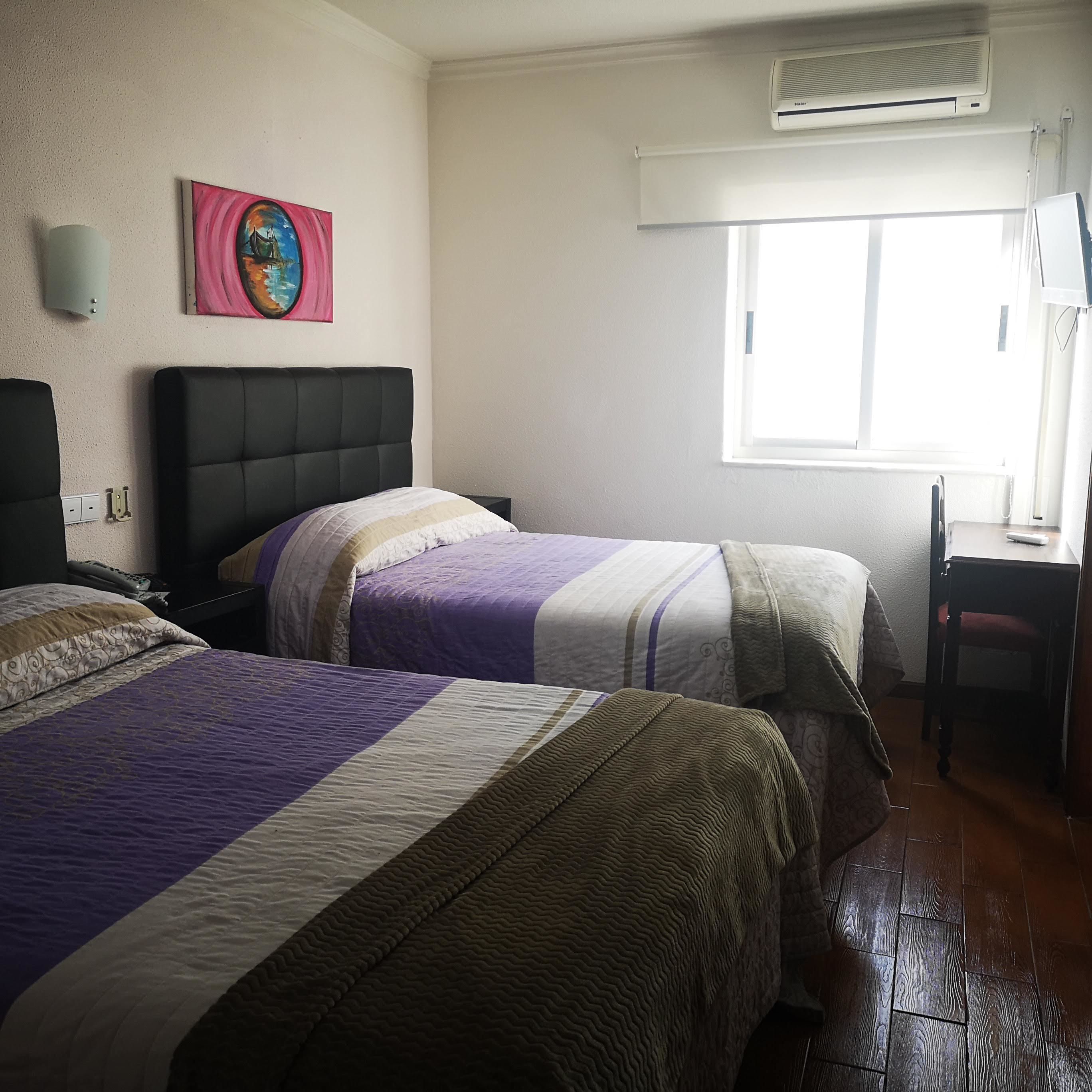 A hotel room with two beds, a desk, and a window.