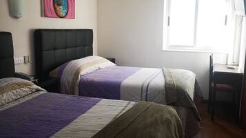 A hotel room with two beds, a desk, and a window.