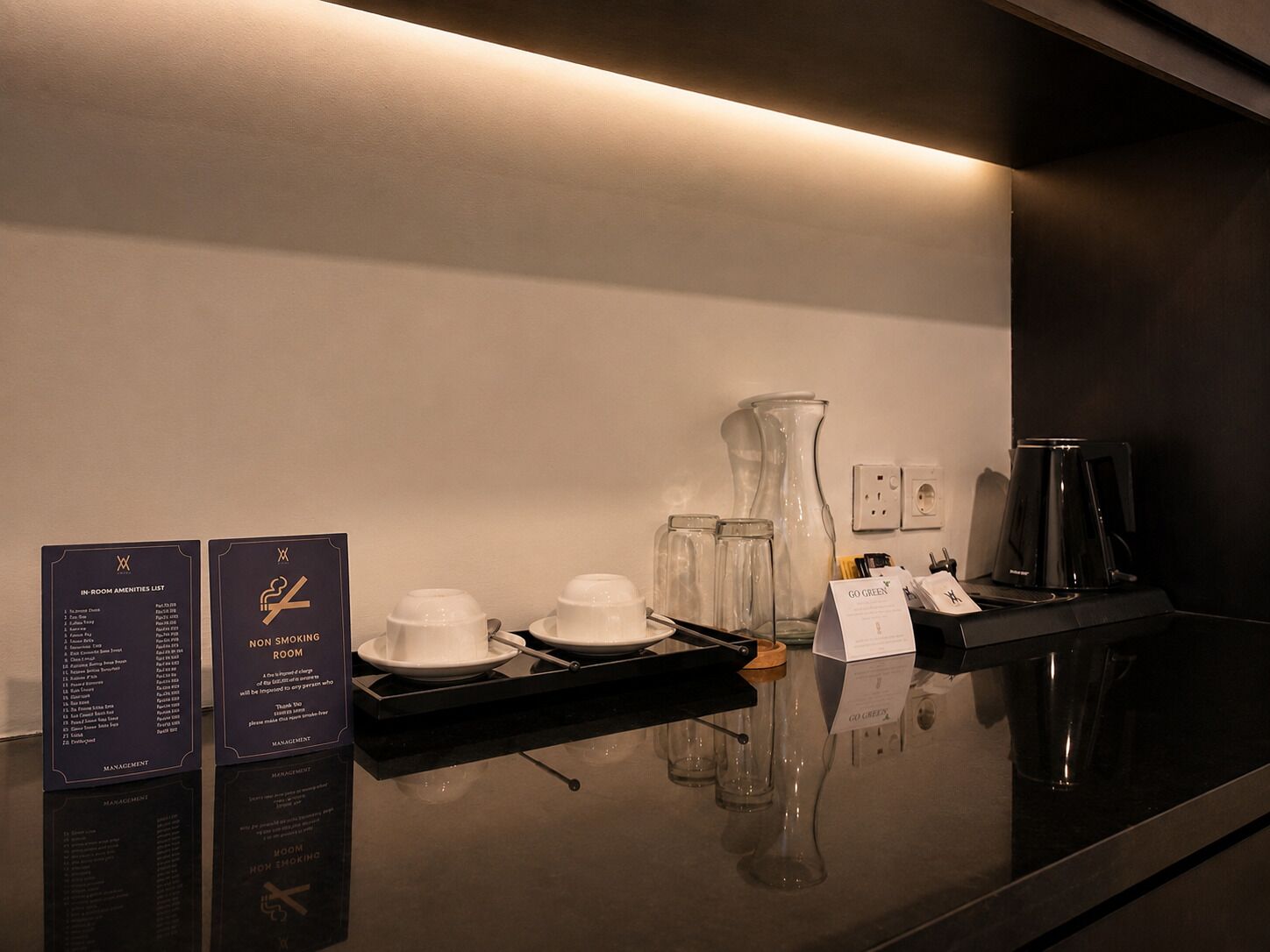 A hotel room with a black countertop, a coffee maker, a sign for non-smoking, and a glass vase.