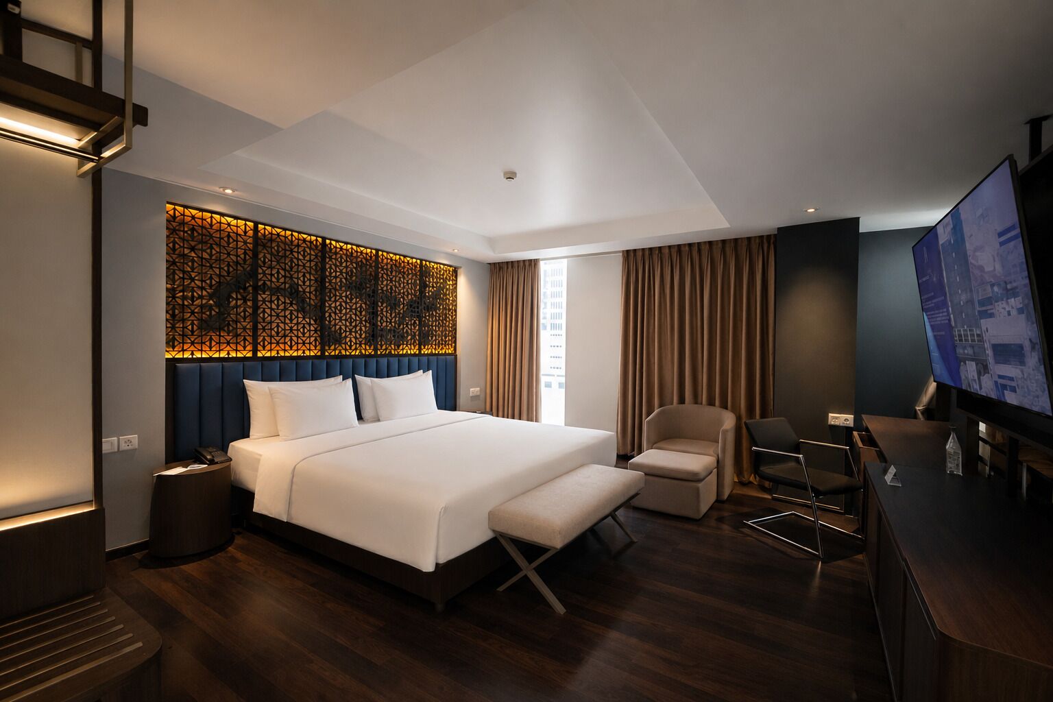 Ein modernes Hotelzimmer mit einem großen Bett, einem Schreibtisch, einem Sessel und einem Fernseher.