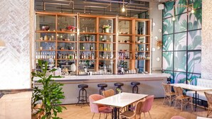 Een bar met flessen en glazen achter een witte toonbank, en zitplaatsen met tafels en stoelen.