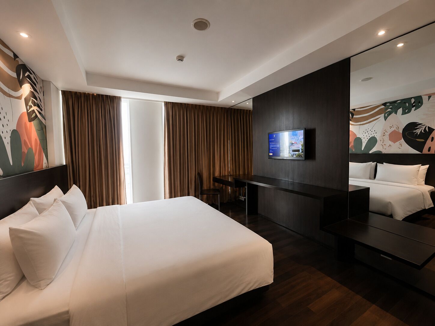 Una habitación de hotel moderna con una cama grande, un escritorio, un televisor y un espejo amplio.